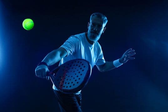 Padel player hitting a forehand under blue court lights